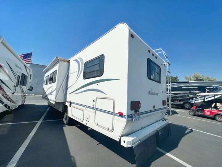 This Coachmen RV rental, with an extended slide-out, awaits adventure on a sunny lot among other motorhomes.. Coachmen Leprechaun 2001