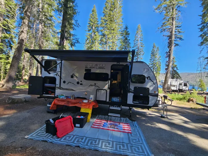 Spacious RV rental in a serene lakeside campsite, complete with tall pines and an inviting outdoor setup.. Cherokee WOLF PUP BLACK LABEL 17JWBL 2025