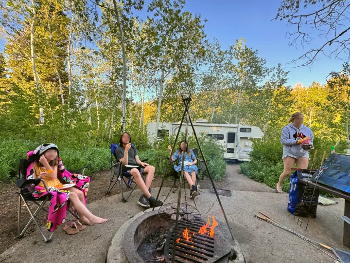 Family grilling burgers at their RV rental campsite. Fire pit is lit for a cozy evening.. Coachmen Leprechaun 2001