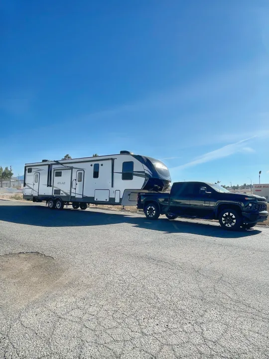 Black pickup truck towing a white Atlas fifth-wheel RV. Your dream rv rental for an amazing road trip!. Dutchmen 3602LFKB 2021