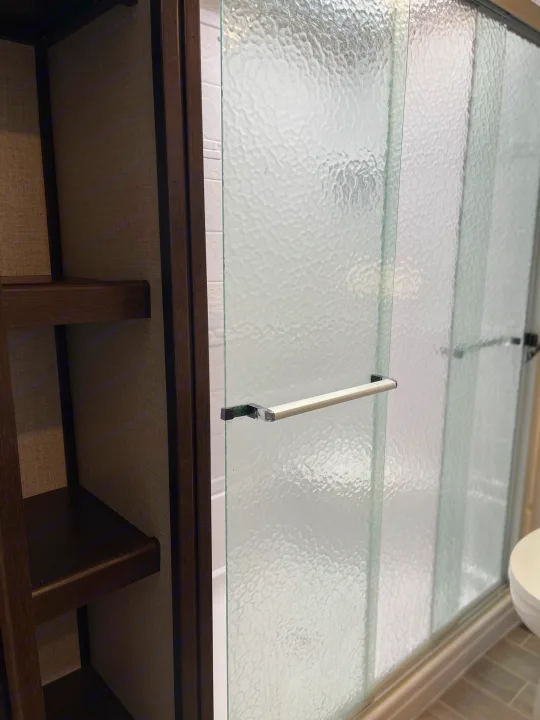 Inside an RV rental: Frosted glass shower doors, wooden shelving, and a white toilet.. Dutchmen 3602LFKB 2021