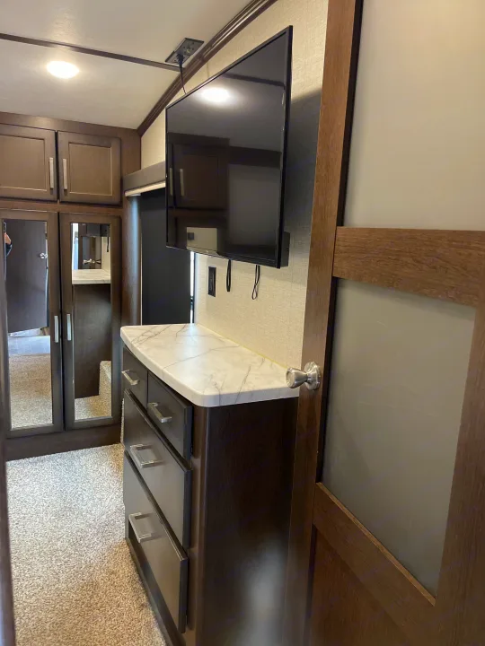 RV rental interior: bedroom area with wall-mounted TV, marble-top dresser, and mirrored closet for storage.. Dutchmen 3602LFKB 2021