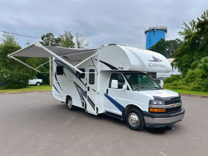 White Chateau Class C RV with extended awning, ideal for rv rental road trips. A blue water tower is in the background.. Thor Chateau 2019