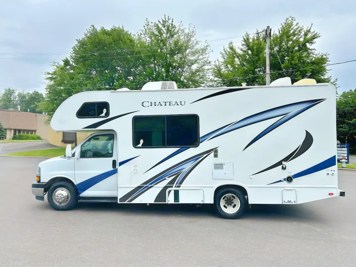 White "CHATEAU" Class C RV rental, parked. Features blue/black graphics, with two whimsical white geese peeking from windows.. Thor Chateau 2019
