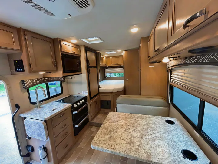 This RV rental interior showcases a full kitchen, dining area, and cozy bed, ready for your next travel adventure.. Thor Chateau 2019
