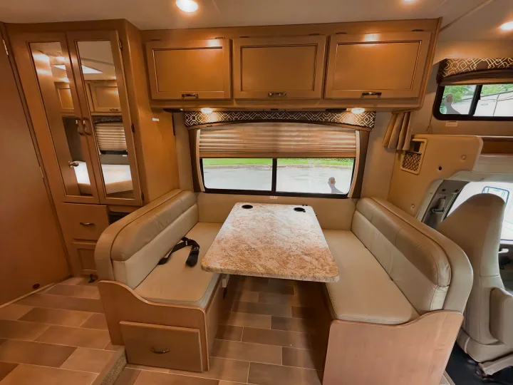 This RV rental features a well-lit dinette area with padded benches, a table, and wooden overhead cabinets.. Thor Chateau 2019