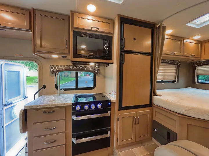 Spacious RV rental interior featuring a full kitchen (sink, stove, microwave, fridge) and a comfortable bed. Ideal for travel adventures.. Thor Chateau 2019