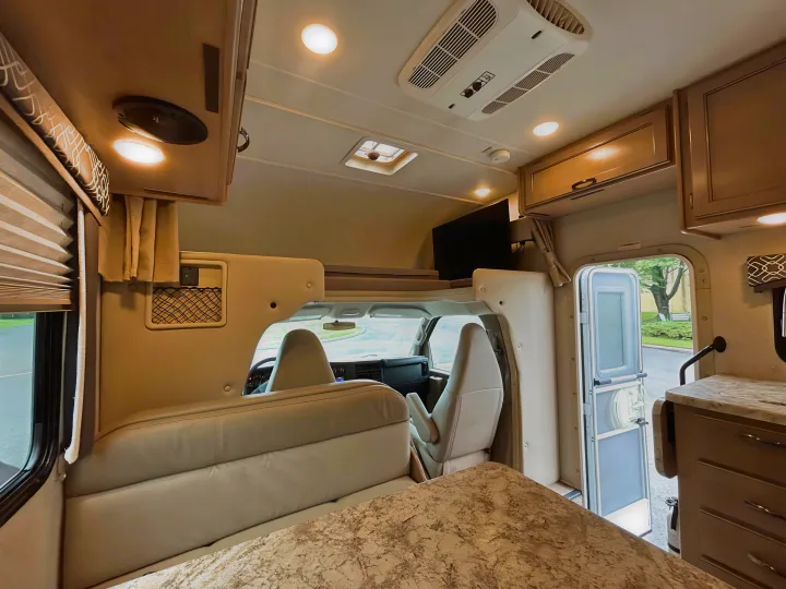 Inviting RV rental interior: comfortable living space with bed, overhead storage, TV, and driver's cabin view.. Thor Chateau 2019