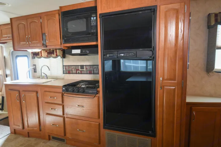 Explore an RV rental's well-equipped kitchen with wood cabinets, microwave, stove, sink, and large refrigerator.. Monaco Safari 2009
