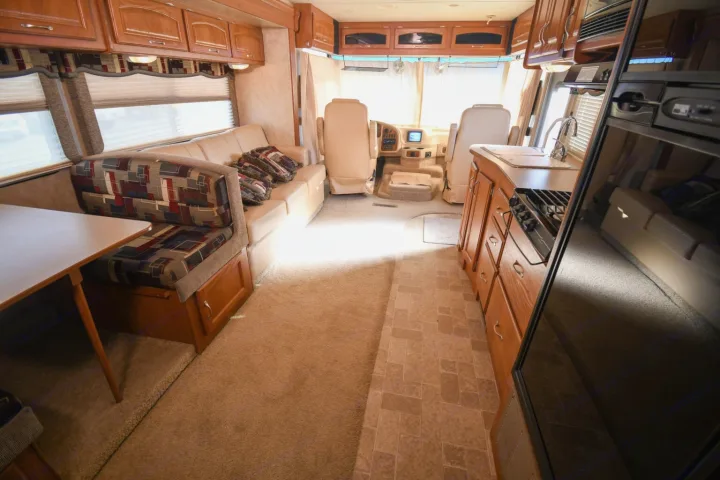 Inside this RV rental: a bright, spacious living area with a dinette, sofa, and kitchen. View extends to the driver's cab.. Monaco Safari 2009