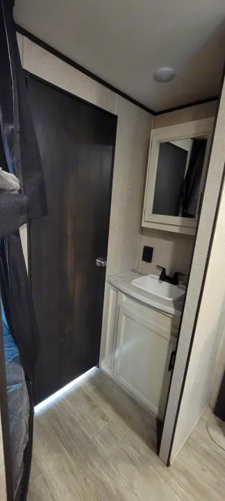 RV rental bathroom: sink, vanity, mirror, and dark wood door. Light walls and floor. Compact travel space.. Jayco Jayco Rocky Mountain 2022
