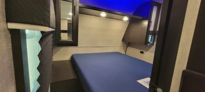 An **RV rental** bedroom with a blue mattress, overhead lights, a window with blinds, and blue ambient ceiling lighting.. Jayco Jayco Rocky Mountain 2022