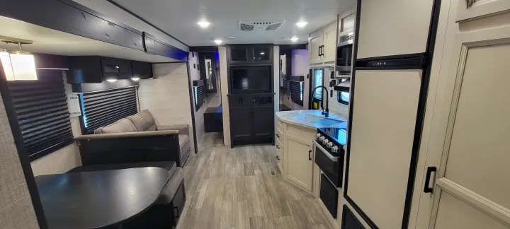 Inside a spacious RV rental: modern kitchen, living area with sofa, and dining table, all with light wood-look flooring.. Jayco Jayco Rocky Mountain 2022
