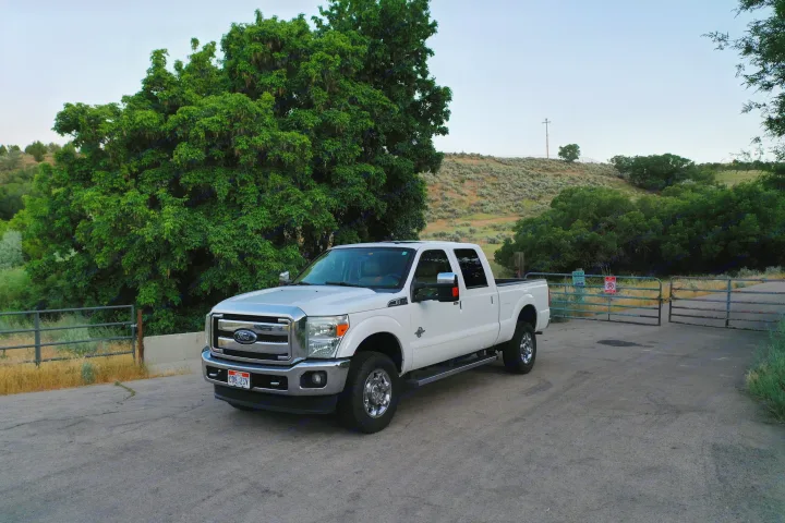 White Ford Super Duty truck on a paved road with trees and hill. Great for towing an RV rental on adventures.. Sportchassis Sportchassis Tow Vehicle 2012