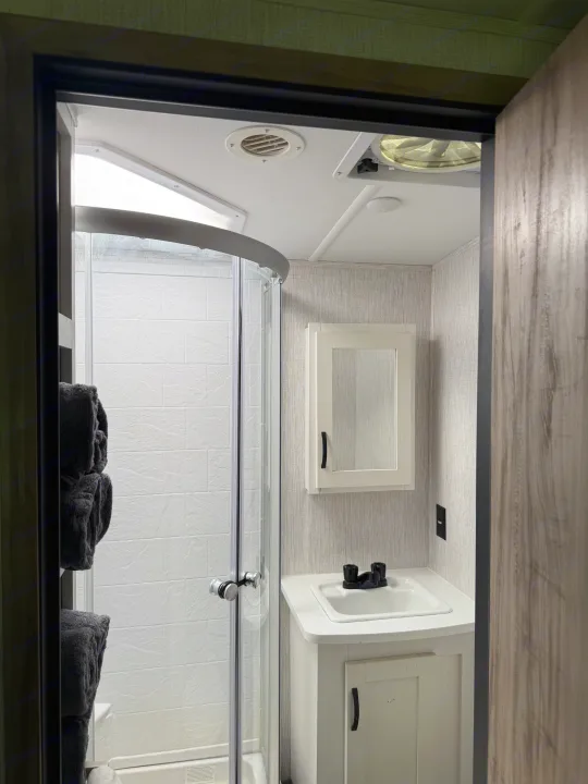 Inside this modern RV rental: a compact bathroom featuring a shower, vanity, sink, and mirrored medicine cabinet.. Palomino SolAire 320 TSBH 2022