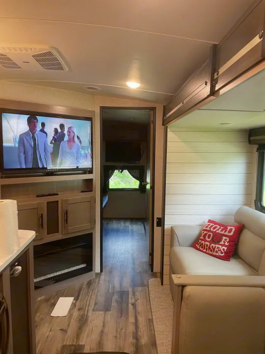 Inside a modern **rv rental**, showing the living area with TV, sofa, electric fireplace, and a hallway leading to bunks. Ideal travel comfort.. Crossroads RV Sunset Trail Super Lite 2023