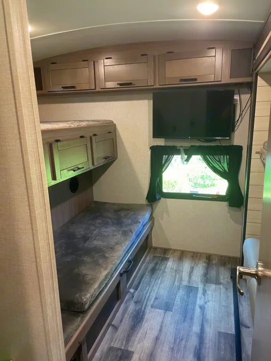 RV rental bunk room with lower bed, overhead cabinets, mounted TV, and window. Designed for comfort.. Crossroads RV Sunset Trail Super Lite 2023