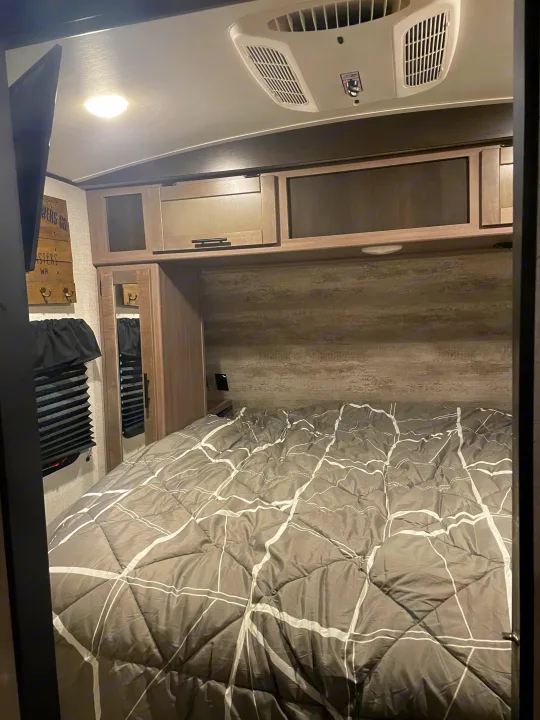 Comfortable RV rental bedroom, featuring a bed with a gray comforter, overhead storage, and AC unit.. Crossroads RV Sunset Trail Super Lite 2023