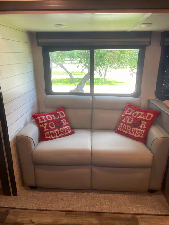 Cozy RV rental interior with a comfy sofa, "Hold Your Horses" pillows, and a scenic window view of trees and grass.. Crossroads RV Sunset Trail Super Lite 2023