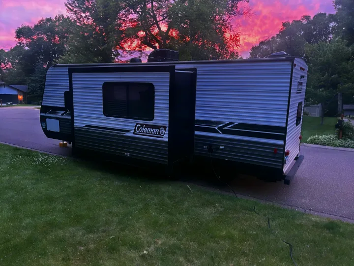 Evening view of a large Coleman RV rental parked roadside with its slide-out extended, under a beautiful pink sky.. Coleman Lantern 242BH 2022