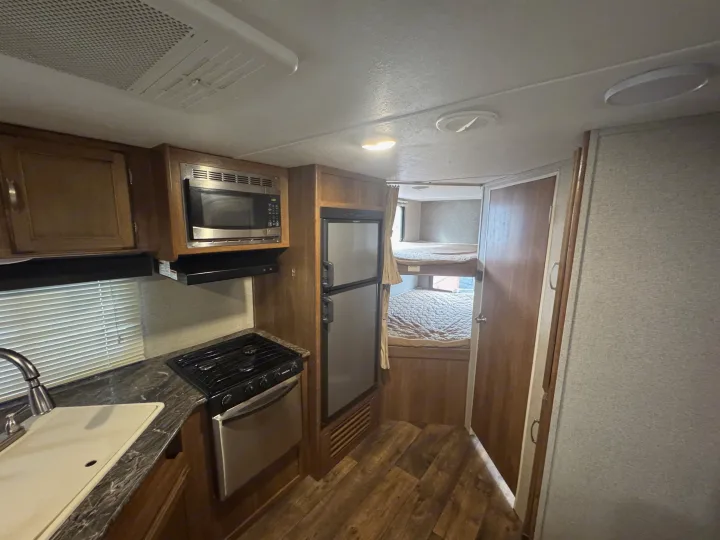Compact rv rental interior featuring a functional kitchen with microwave, stove, fridge, and two cozy bunk beds.. Keystone RV Springdale 2018