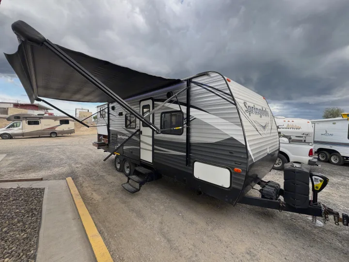 RV rental: Modern Springdale travel trailer camper with awning extended in a dusty lot under cloudy skies.. Keystone RV Springdale 2018