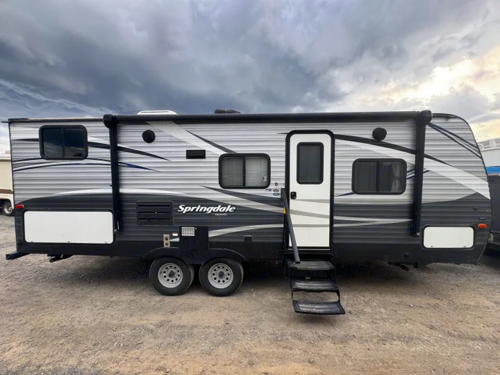 Grey and black RV rental parked on a gravel lot under dramatic clouds.. Keystone RV Springdale 2018