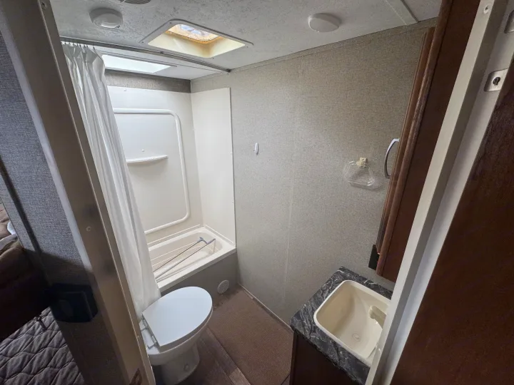 RV rental bathroom with toilet, tub/shower, sink, and overhead skylight. Clean, functional, and ready for your travels.. Keystone RV Springdale 2018