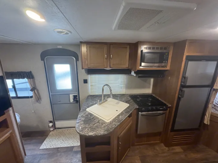 Cozy RV rental interior: kitchen with sink, stovetop, microwave, fridge, and overhead AC unit. Exit door visible.. Keystone RV Springdale 2018