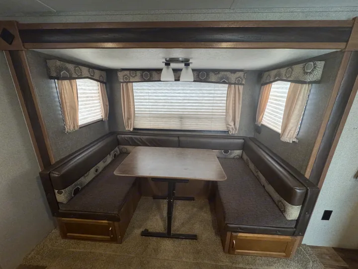 Cozy RV rental dinette features a U-shaped booth, central table, and windows with blinds, ideal for meals or relaxing inside.. Keystone RV Springdale 2018
