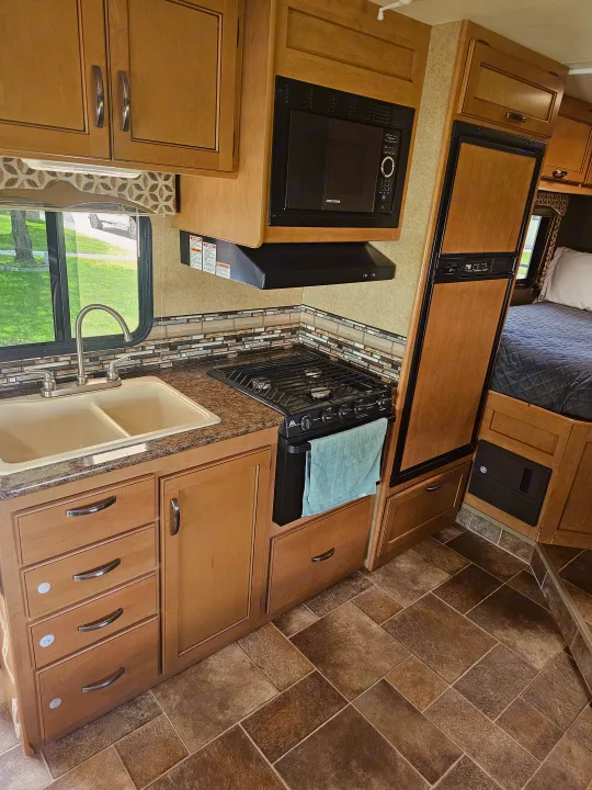 This RV rental features a compact kitchen with a sink, stove, microwave, and refrigerator, plus a bedroom section.. Thor Four Winds 2016