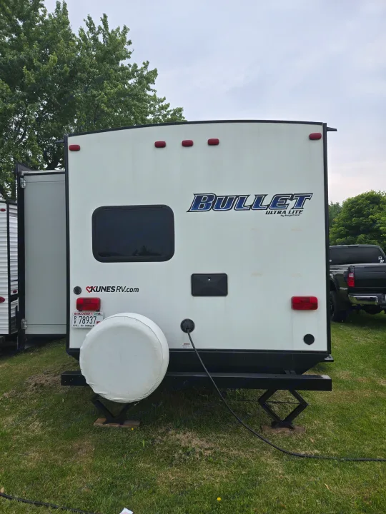 Rear of a white Bullet Ultra Lite travel trailer, ideal for an RV rental, parked on grass with power connected.. Keystone RV Bullet Ultra Lite 2018