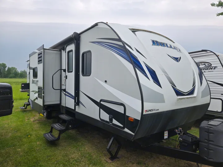 White Bullet travel trailer RV rental with blue accents, parked in a grassy field, slide-out extended.. Keystone RV Bullet Ultra Lite 2018