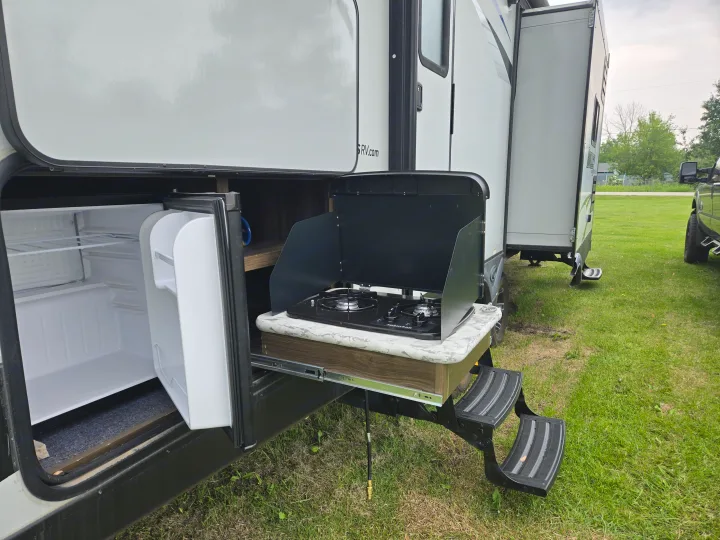 RV rental featuring an outdoor kitchen with pull-out stove, mini-fridge, and convenient steps for easy access.. Keystone RV Bullet Ultra Lite 2018
