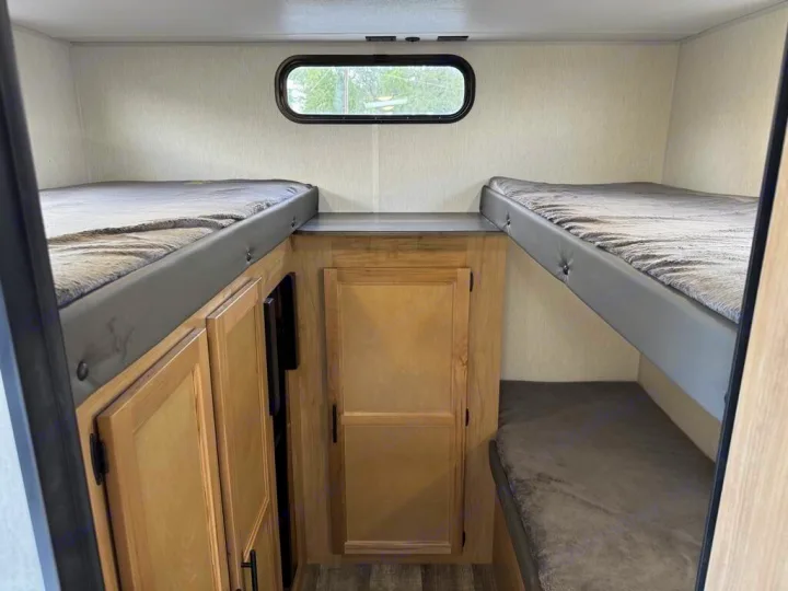 RV rental interior featuring comfortable bunk beds, practical storage cabinetry, and a small window.. Forest River Cherokee Grey Wolf 2023
