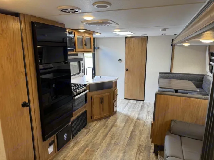 Inside this modern RV rental: a compact kitchen with a large fridge, stove, sink, and a comfortable dinette. Wood flooring throughout.. Forest River Cherokee Grey Wolf 2023