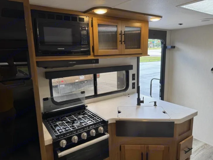 Modern RV rental kitchen with microwave, stove, sink, and ample counter space, perfect for mobile cooking.. Forest River Cherokee Grey Wolf 2023