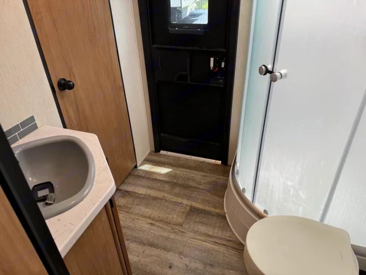 RV rental bathroom features a vanity with sink, compact toilet, and frosted glass shower. Maximizes space.. Forest River Cherokee Grey Wolf 2023