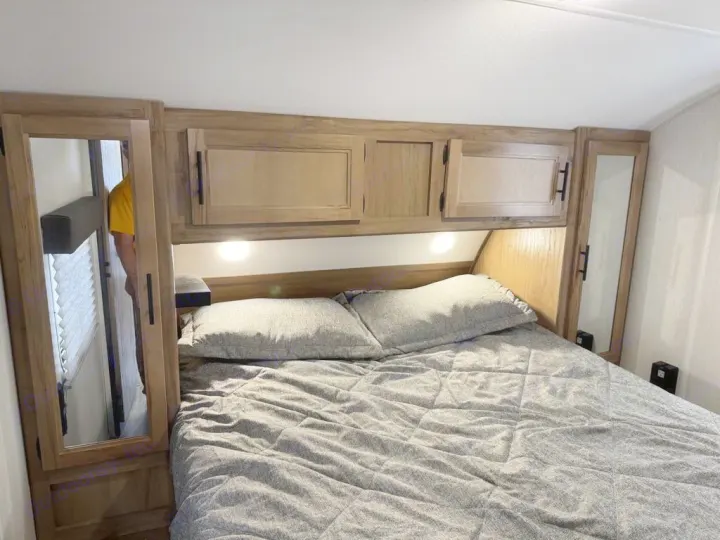 Cozy RV rental bedroom featuring light wood cabinets, under-cabinet lighting, and a grey quilted bed.. Forest River Cherokee Grey Wolf 2023