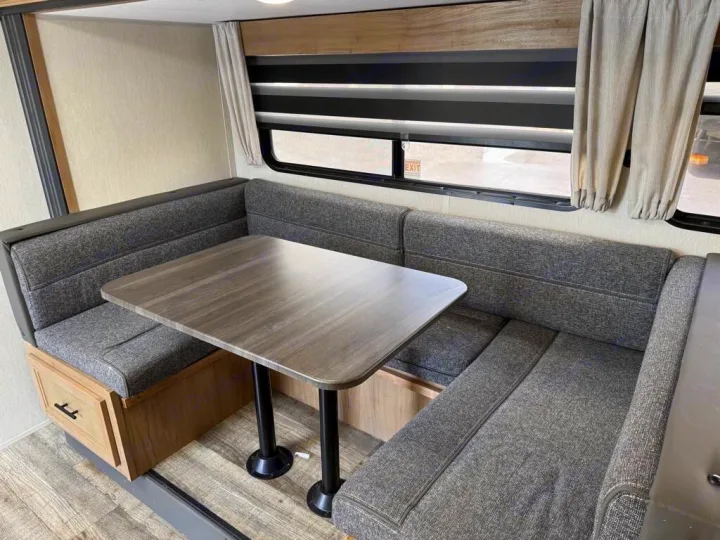 RV rental dinette with U-shaped grey fabric booth seating, a wooden table, and windows with blinds and curtains.. Forest River Cherokee Grey Wolf 2023