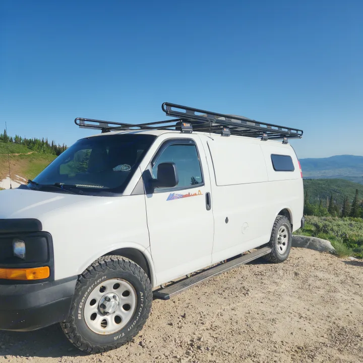 Scenic mountain view behind a white adventure camper van with roof rack, ready for your next rv rental journey.. Chevrolet Express 1500 AWD 2014