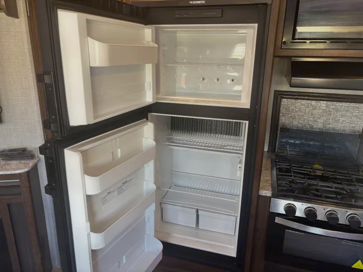 Open Dometic fridge/freezer and Greystone range in a clean RV rental kitchen, ready for use.. Crossroads RV Zinger 2020
