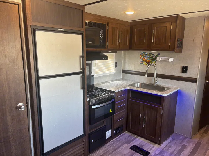 RV rental interior: a fully equipped kitchen with a large refrigerator, microwave, stove, sink, and wood cabinets.. Crossroads RV Zinger 2020