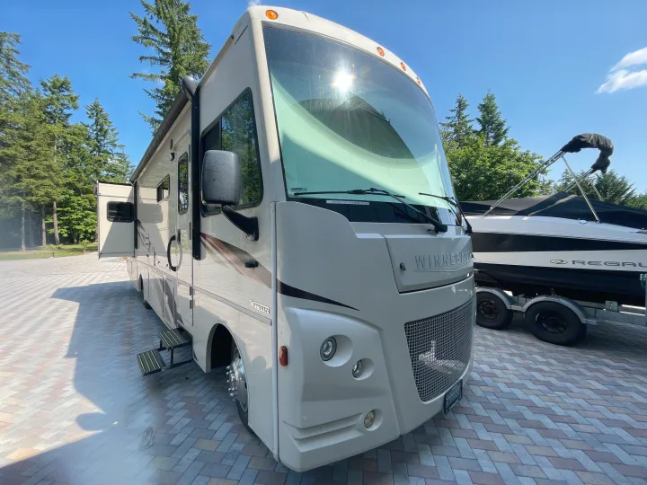 A large cream Winnebago motorhome RV, an excellent rv rental option, is parked on a patterned driveway with a boat.. Winnebago Vista 2019