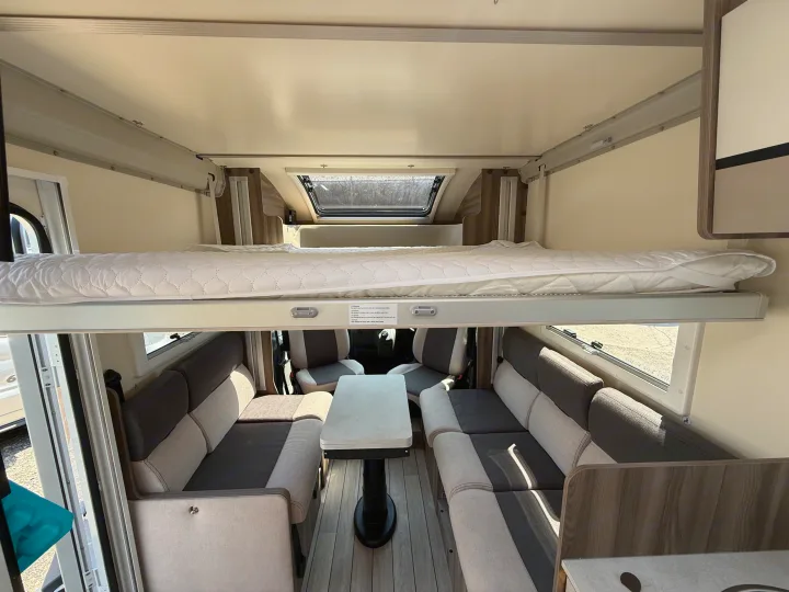 This RV rental interior features a cozy drop-down bed over a comfortable living area with seating and a table.. Rollerteam Kronos Compact 590 2026
