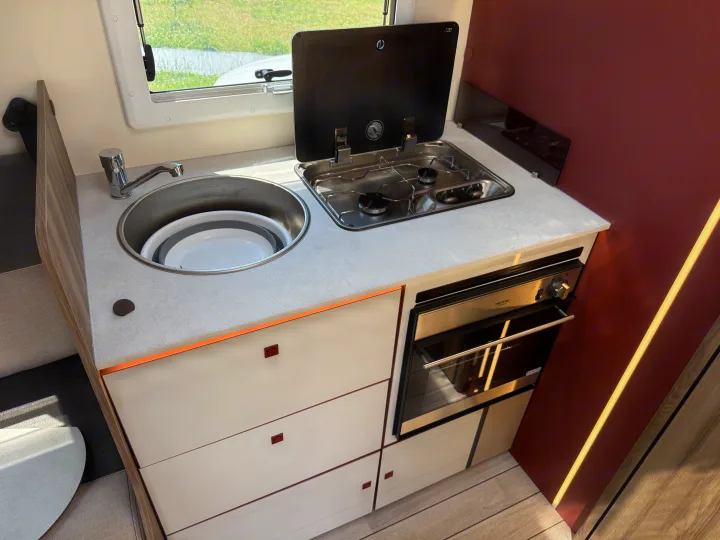 RV rental's compact kitchen area: chrome sink, two-burner stove with cover, and built-in oven below.. Rollerteam Kronos Compact 590 2026