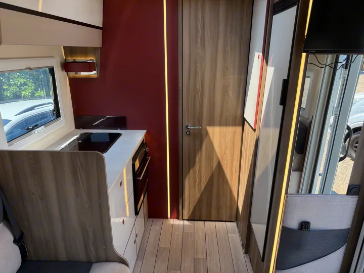 Modern RV rental interior with a compact kitchen, wooden finishes, and warm accent lighting, showcasing efficient space.. Rollerteam Kronos Compact 590 2026