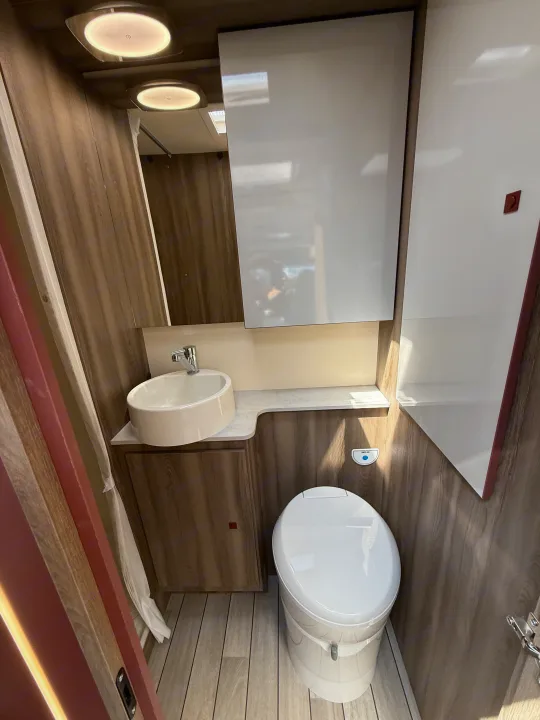 This clean RV rental bathroom features a white toilet, vessel sink, and modern lighting, set against warm wood-look walls.. Rollerteam Kronos Compact 590 2026