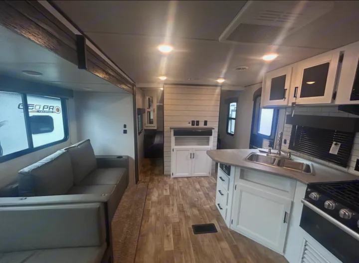 Spacious rv rental interior: bright living room with couch, full kitchen, & wood-look floor. Ready for adventures!. Keystone RV Hideout 2023