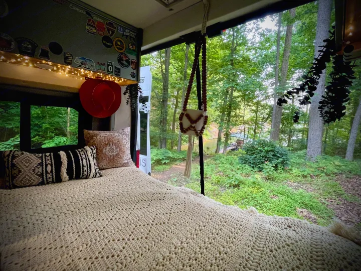 Cozy RV rental interior with a bed looking out to a serene forest and lake view. Perfect for nature lovers!. Dodge Winnebago 2021